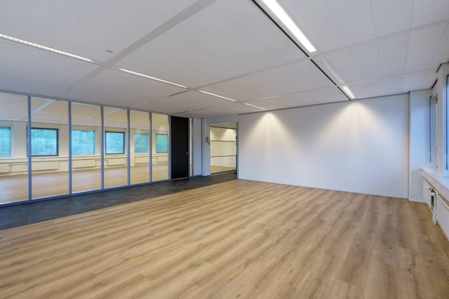 Licht en modern kantoorinterieur aan de Baarnsche Dijk met houten vloer en glazen scheidingswand.